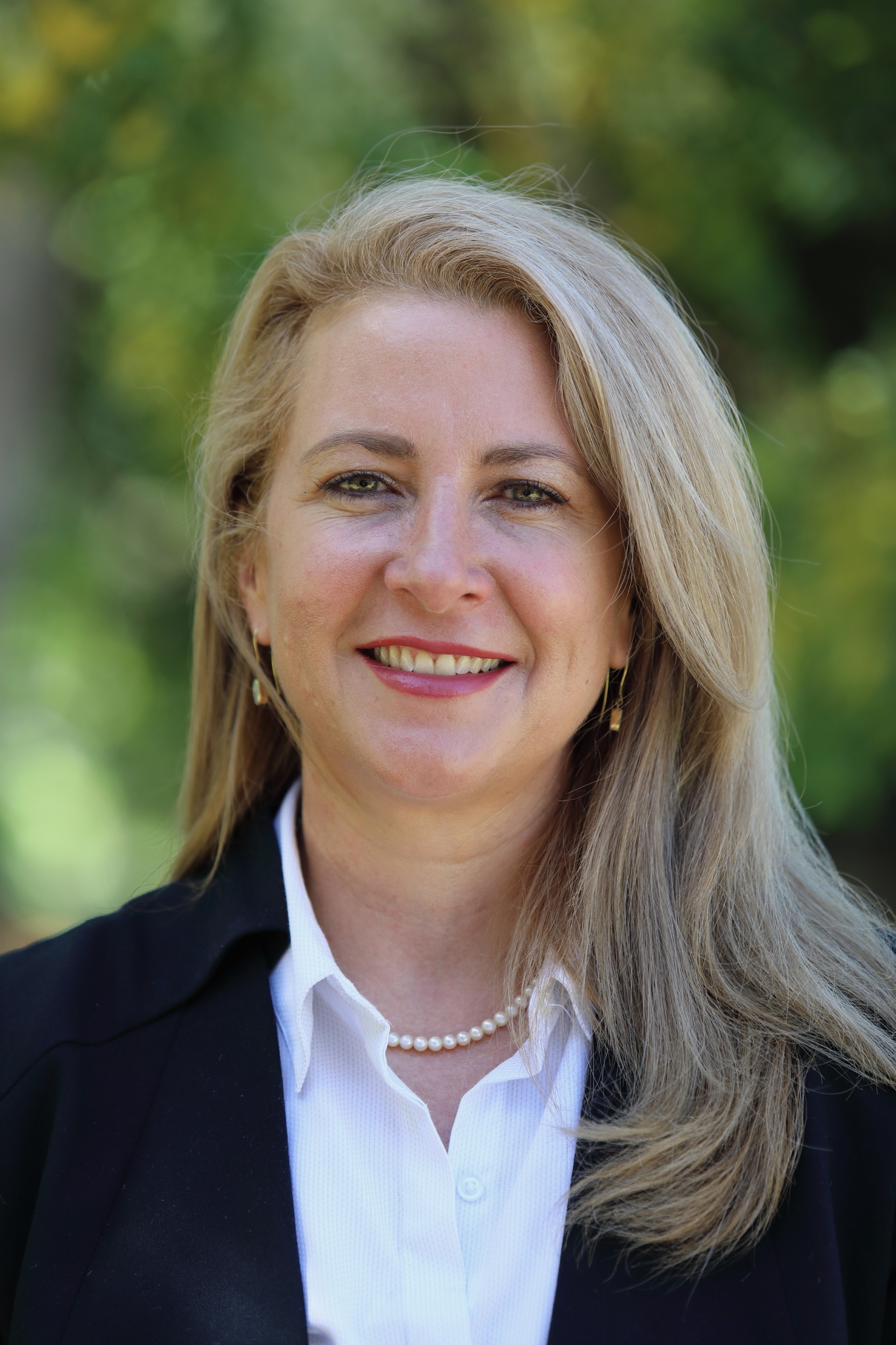 A woman with blonde hair in a headshot with leafy green background