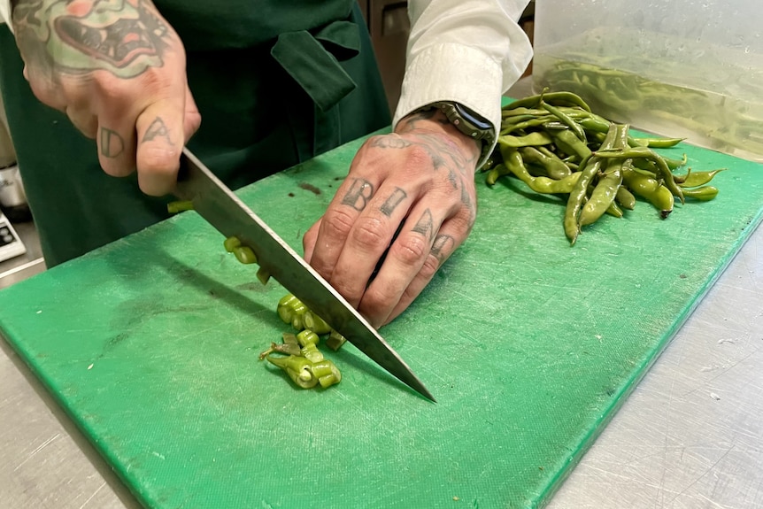 A pair of tattooed hands chopping up greens on a chopping board.
