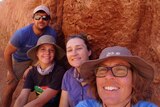 Four people smile in front of a termite mound.