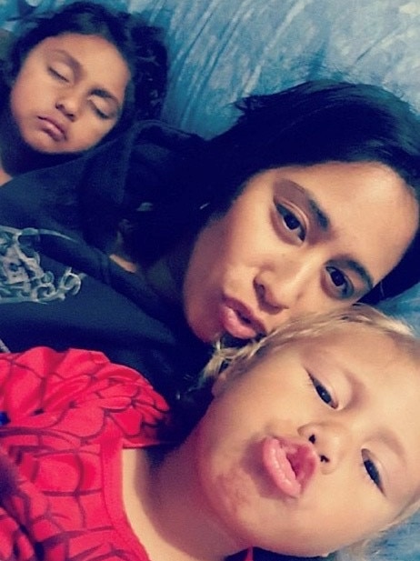 A woman and her son and daughter take a selfie lying in a bed.