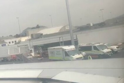 Ambulances are visible on the tarmac in a blurry photo taken from a plane window.