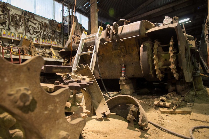 A rusted tank body with parts lying around on a dusty shed floor