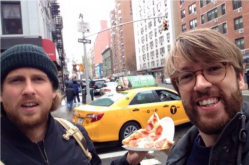 Two men on a NYC street holding a slice of pizza