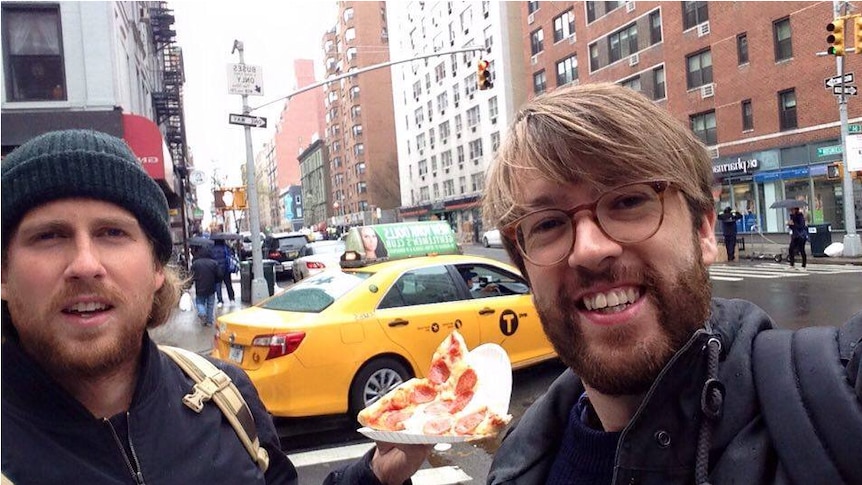 Two men on a NYC street holding a slice of pizza