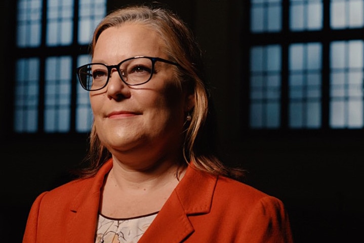 A woman wears glasses and an orange jacket.