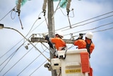 Two power workers in a cherry picker work to repair a power pole.