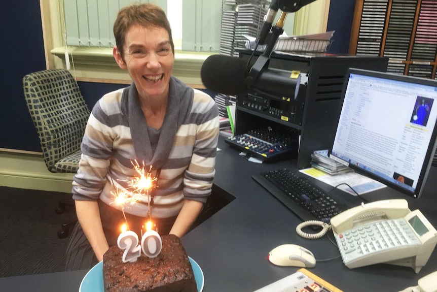 A woman in a radio studio smiling with a cake.