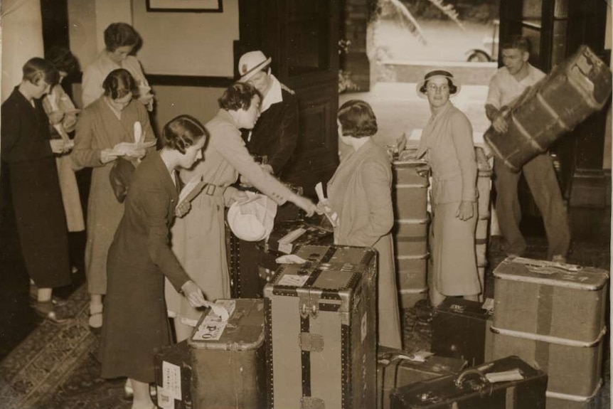 A black and white photograph of the English Women's Cricket Team with their luggage, in a foyer.
