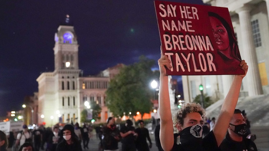 Protesters march in Louisville as one man holds a sign that says "say her name Breonna Taylor".