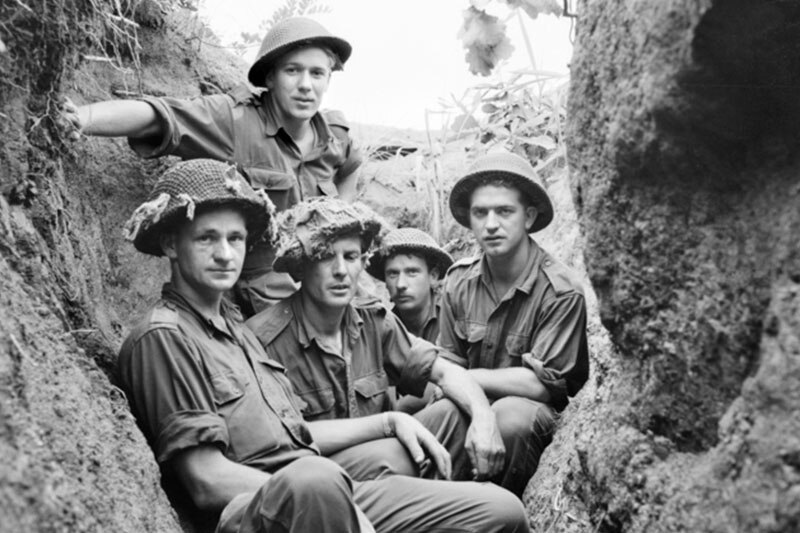 Black and white image of five soldiers in a trench looking at the camera