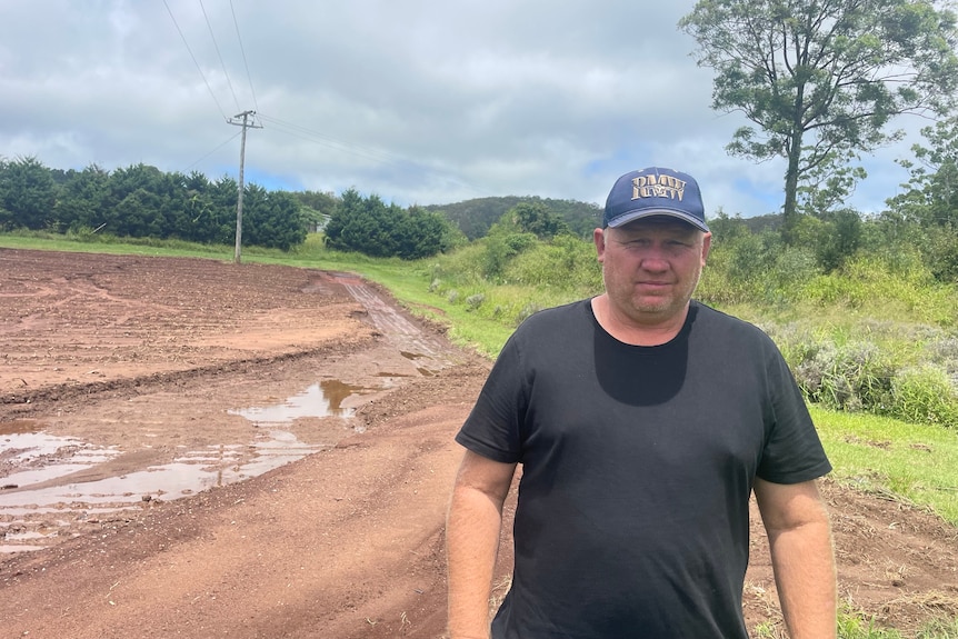 A man stands in front of a field that is all gouged out by floodwater.