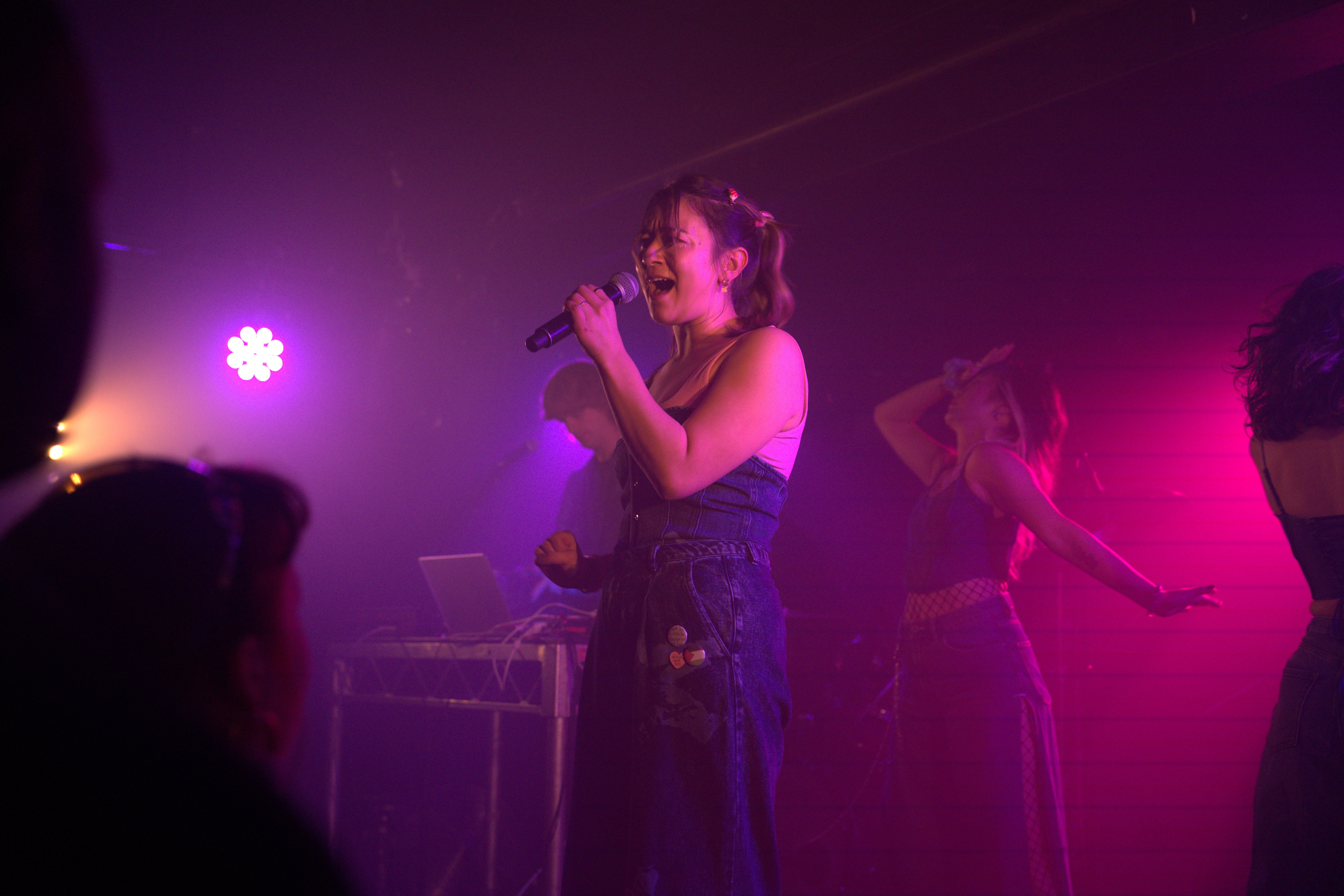 Emi Doi stands on stage with two dancers and holds a microphone.