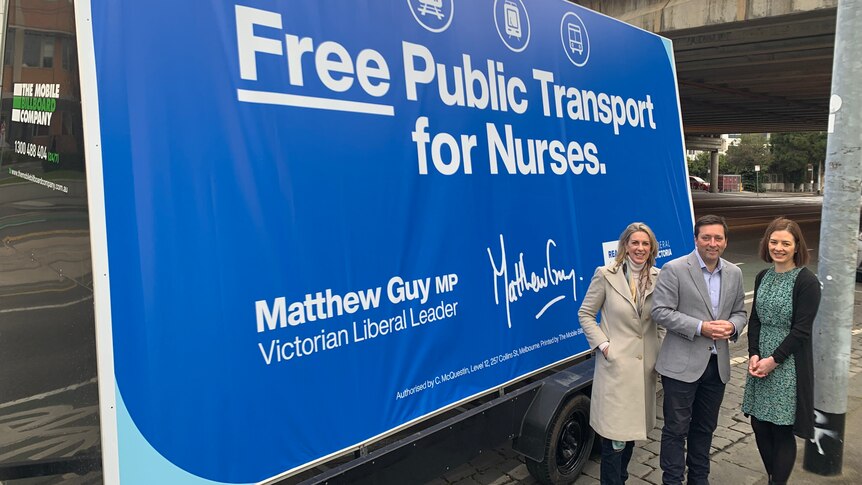 Georgie Crozier, Matthew Guy and Renae Guy stand by a blue billboard reading 'Free Public Transport for Nurses'.