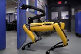 Boston Dynamics' SpotMini robot opens a door with a mounted mechanical claw.