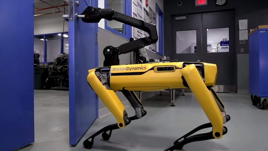 Boston Dynamics' SpotMini robot opens a door with a mounted mechanical claw.