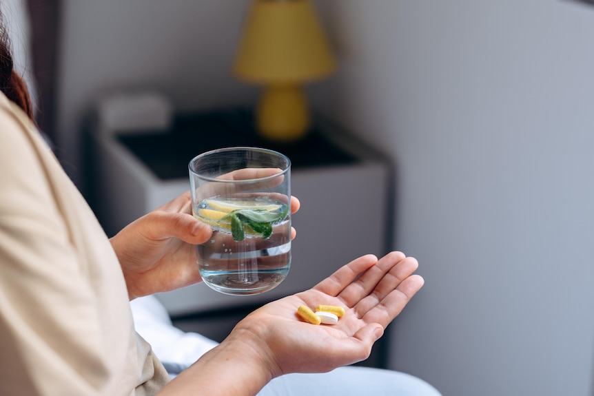 Woman sitting on bed with pills in one hand, water with lemon slice in the other