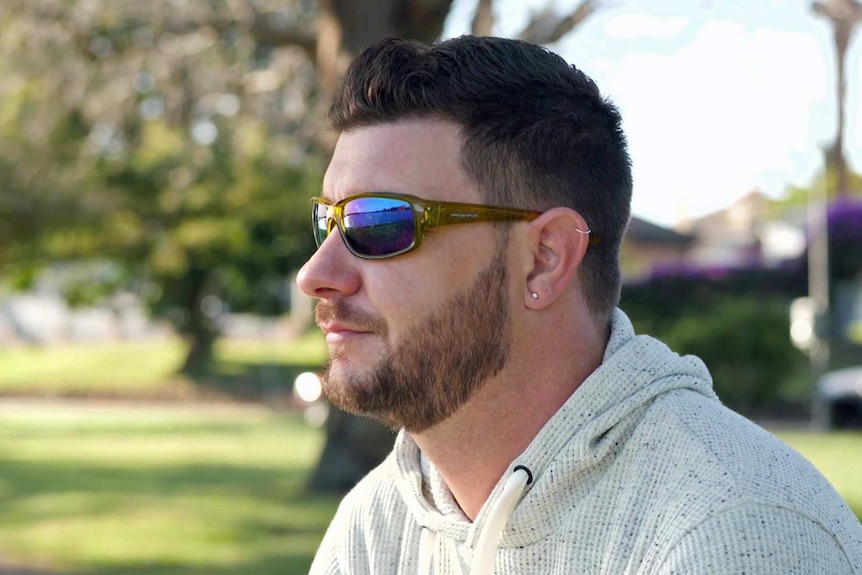 A man wears sunglasses and a grey hoodie.