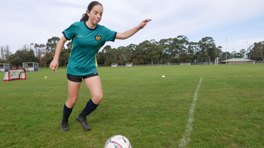 A girl wearing an Australian soccer top kicking a ball