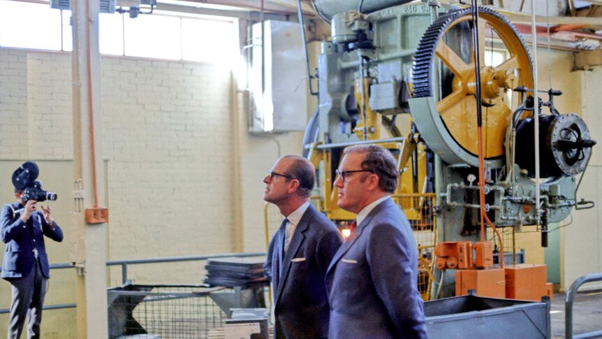 A 1970s colour photograph of Prince Phillip and another man in suits in a factory