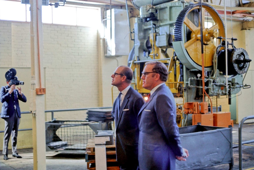 A 1970s colour photograph of Prince Phillip and another man in suits in a factory