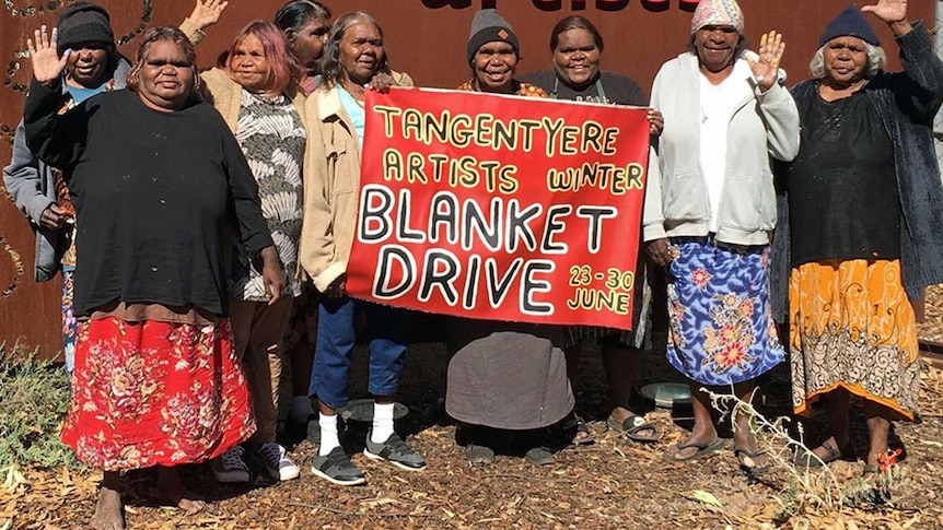 Woman stand in front of a banner promoting blanket drive