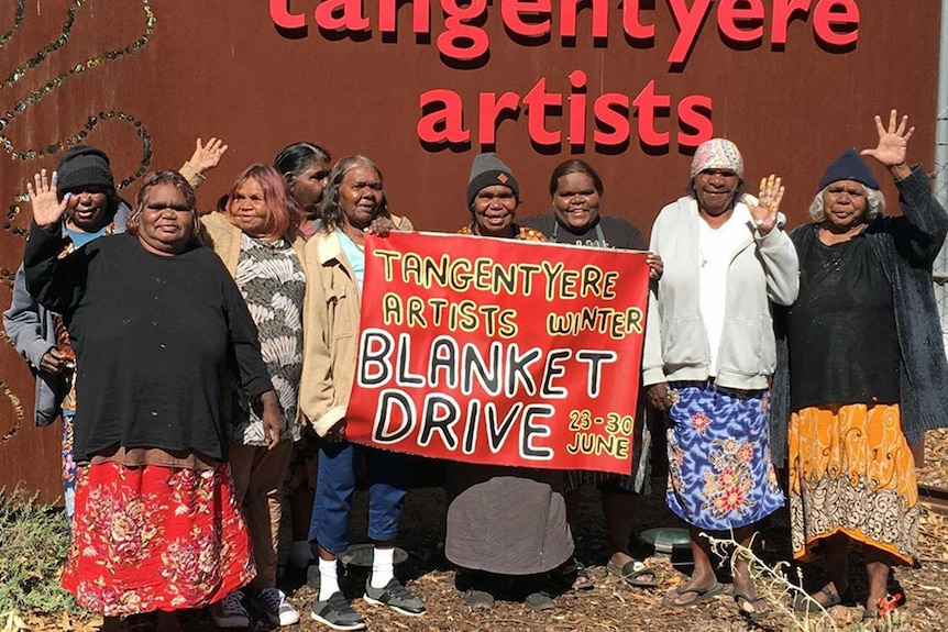 Woman stand in front of a banner promoting blanket drive.