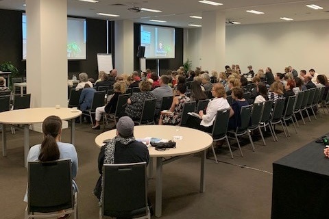 A group of people sitting on chairs facing a screen at a conference