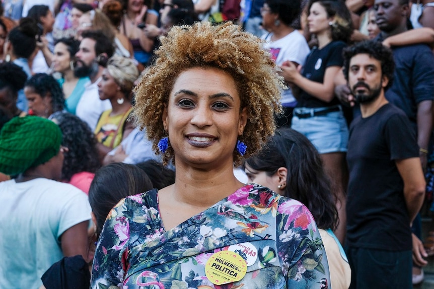 A woman smiles as she poses for a photograph in front of a large crowd