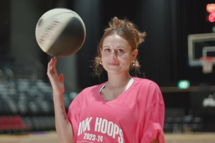 Tiana Mangakahia is wearing a pink t-shirt that says 'pink hoops', she's spinning a basketball on her finger and smiles.
