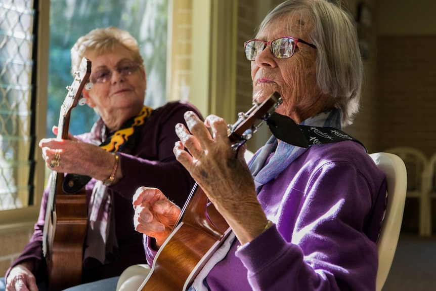 Two elderly women play the ukulele