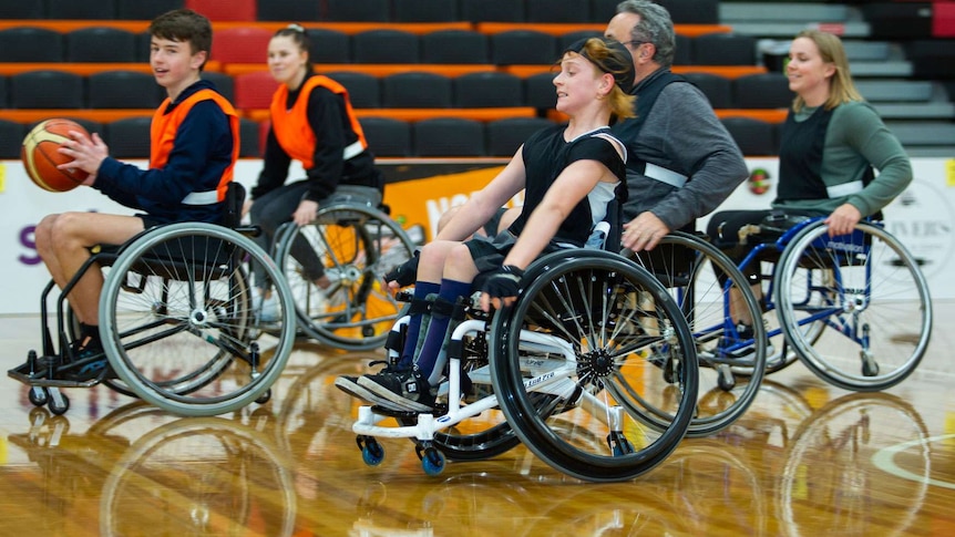 Wheelchair basketball players stream down the court, chasing the ball carrier