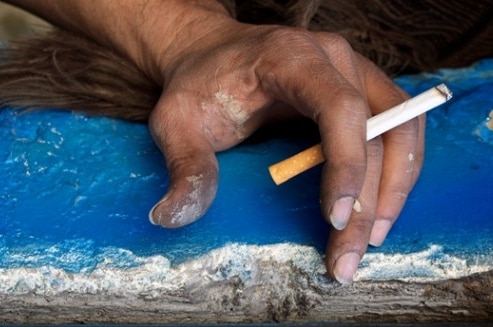 A close-up of an Indigenous person's hand holding a cigarette.