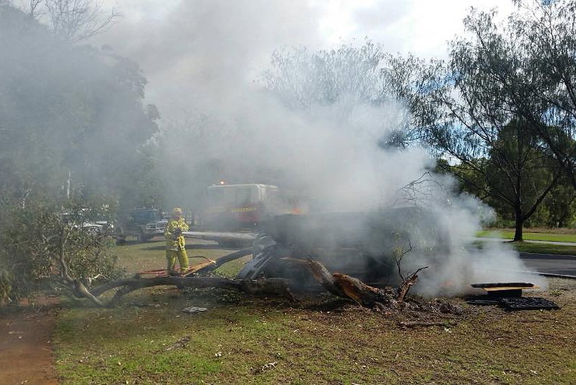 A firefighter hoses a burning car which has flipped on its side, as a smoke plume rises.