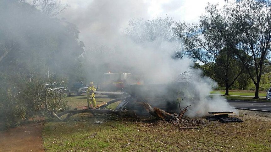 A firefighter hoses a burning car which has flipped on its side, as a smoke plume rises.