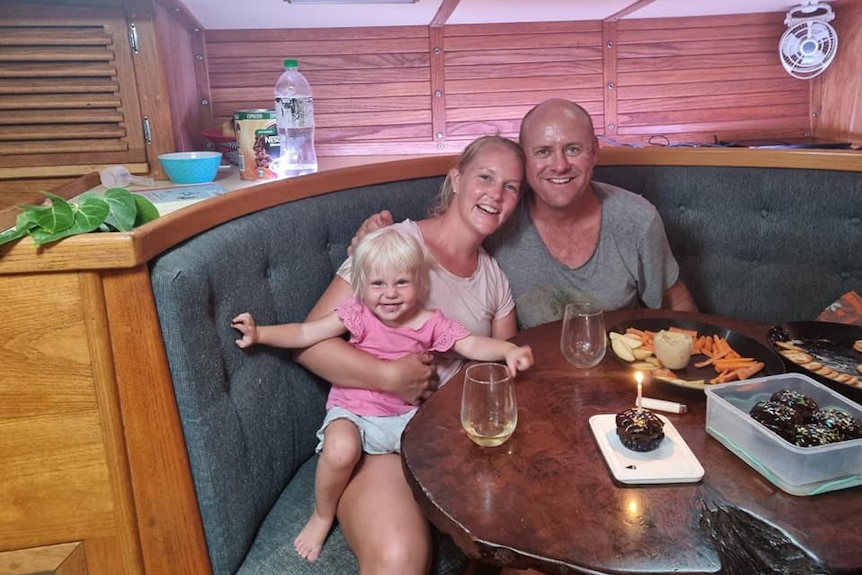 A picture of a woman in her 30s, a man in his 40s, and a toddler sitting at a dinner table in a boat's cockpit.