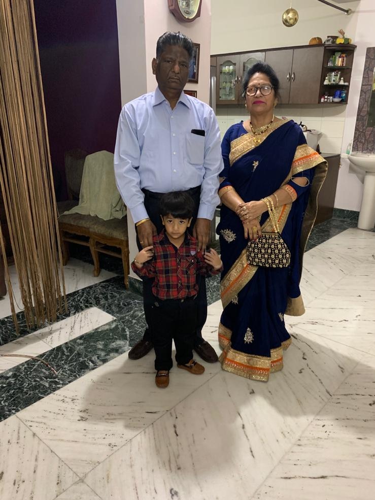 An older man and a woman in a saree standing in a living room with a toddler in front.