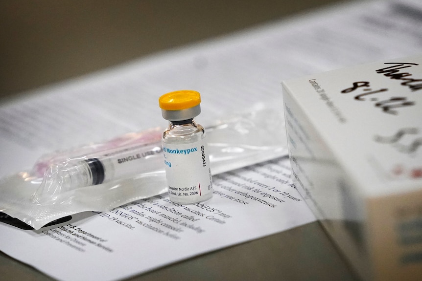 A vial of the Monkeypox vaccine sits on a table next to a syringe.