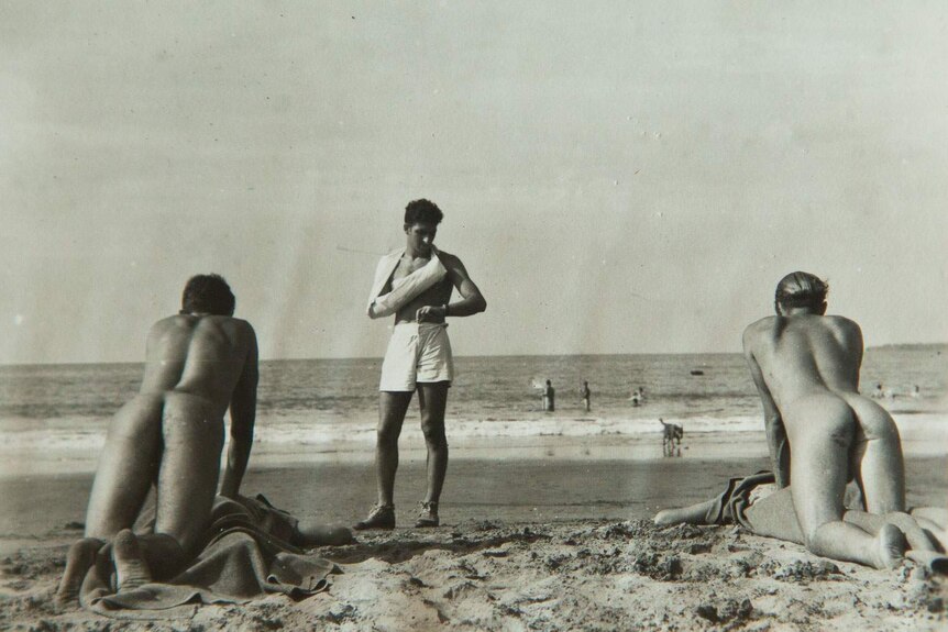 Historic image of naked soldiers, photographed back on, practicing CPR on mock patients on a beach