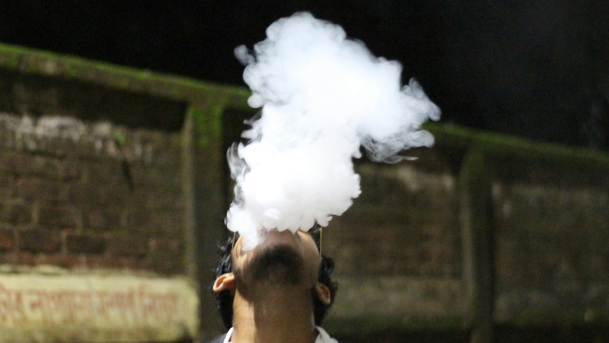 A man vaping tilts his head upwards as a plume of smoke rises from his mouth and nose.
