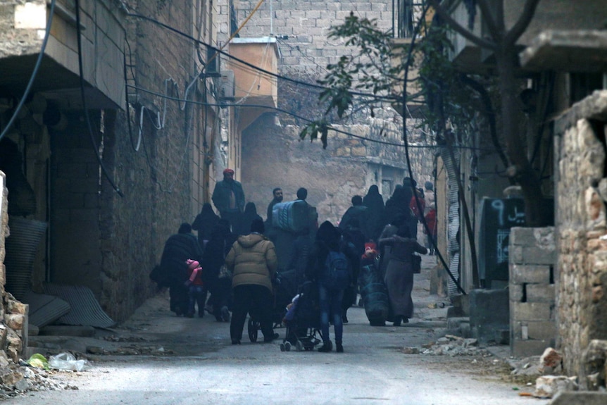 People carry belongings as they flee down a street.