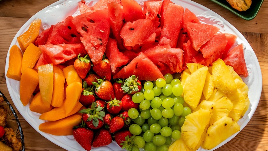 Close up of a plate of cut fruit including strawberries, grapes, pineapples, watermelon and pawpaw.