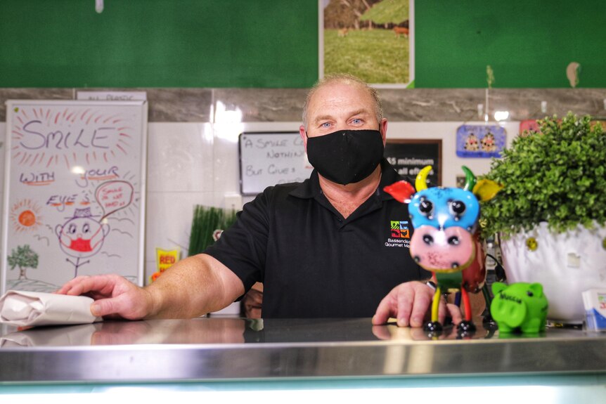 Paddy Sims hands a package of meat across the counter while wearing a mask