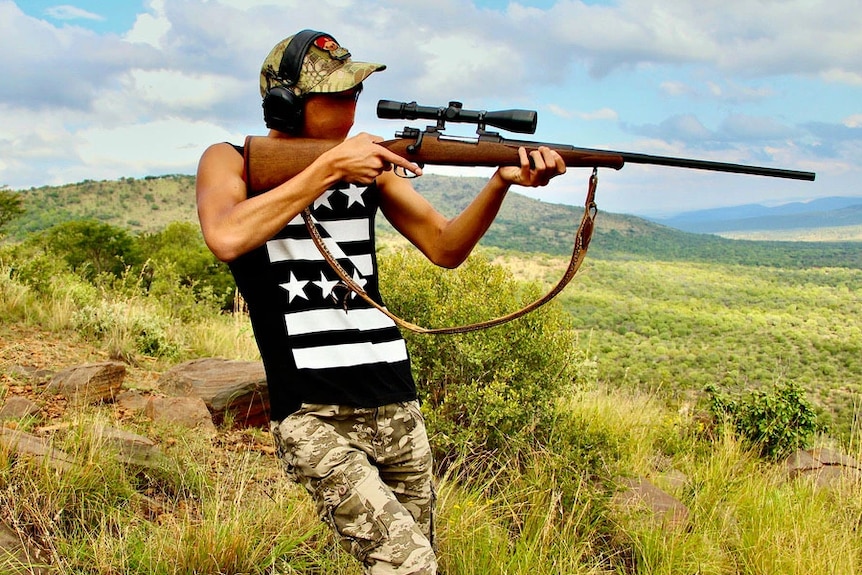 Man standing in bush aiming a rifle.