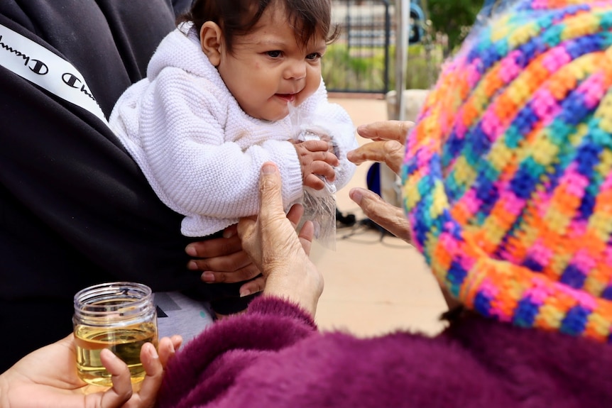 An old Aboriginal lady smearing olive oil and ochre on a baby's forehead. 