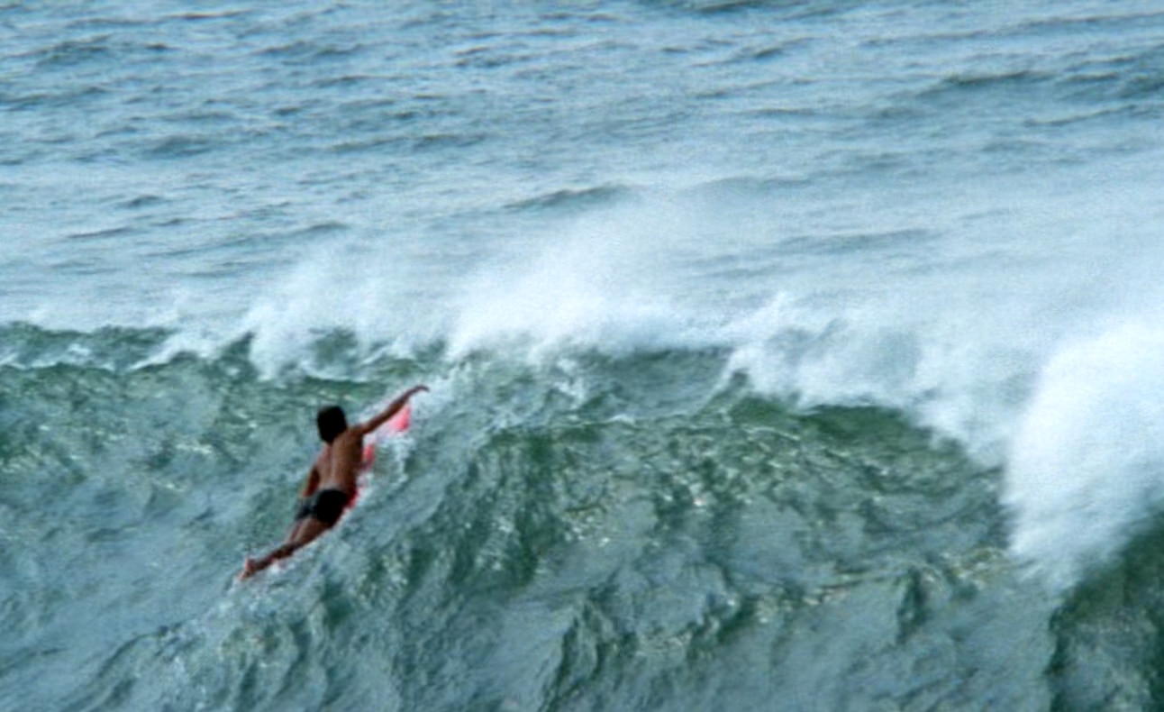 Um surfista rema na beira de uma grande onda.