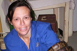 A dark-haired woman in blue scrubs holding a python.
