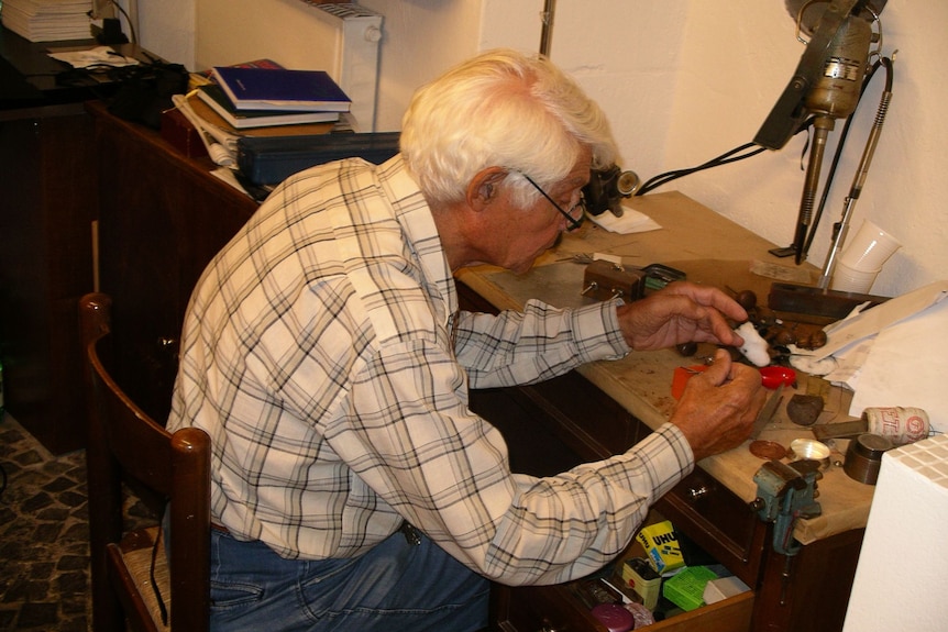 A man with white hair and glasses works with his hands.