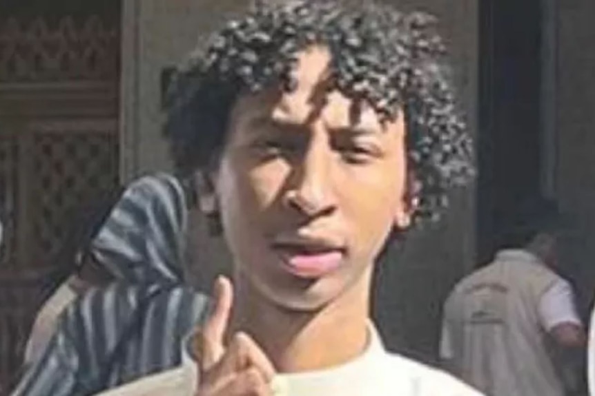 A photo of Hashim Mohamed, who has curly black hair and is holding up a hand.