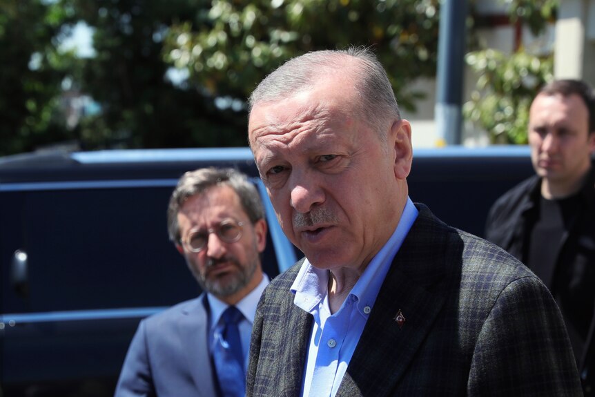 Turkish President Recep Tayyip Erdogan speaks to media as he stands in front of a car.