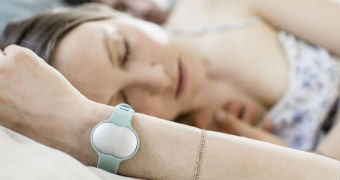 A woman lies on a bed with her eyes closed while wearing the Ava fertility tracking bracelet.